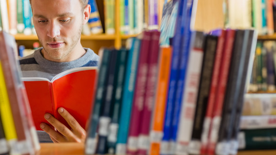 Männlicher Student liest ein Buch in der Bibliothek
